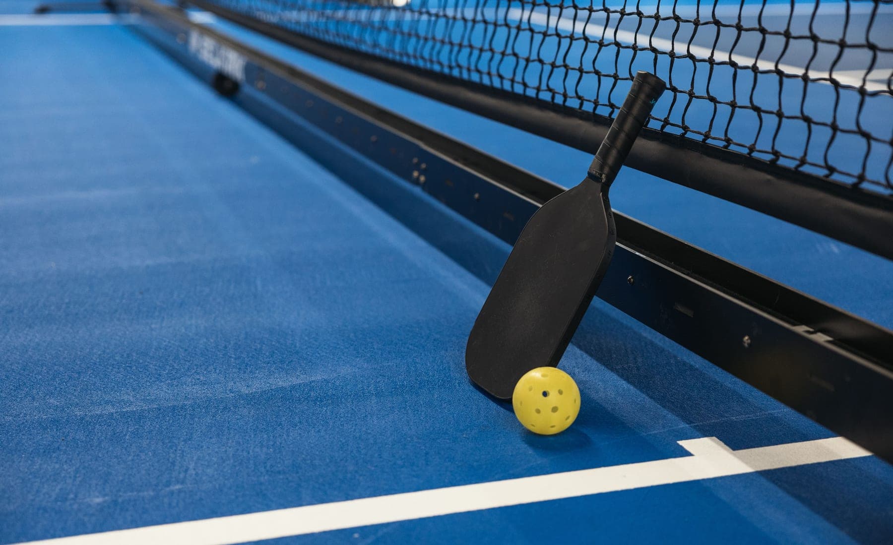 Pickleball paddle and perforated ball on a painted outdoor court