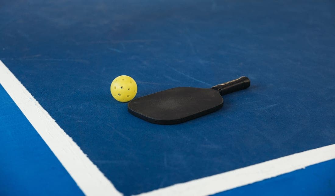 Pickleball paddle and perforated ball on a painted court surface