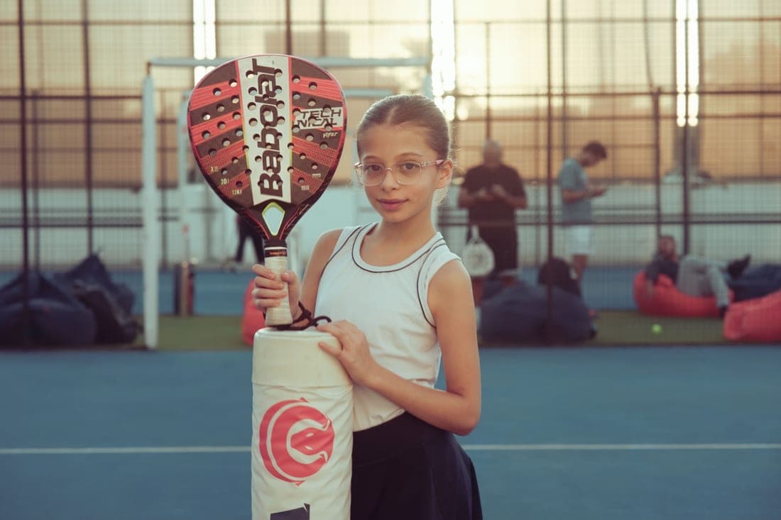 Perforated padel racket face resting against a glass court wall